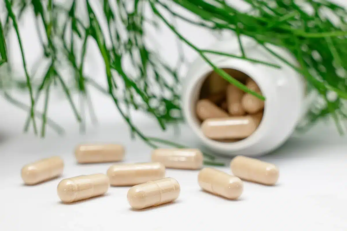 Bouteille de complément alimentaire ouverte avec capsules et verre d'eau sur un plan de travail