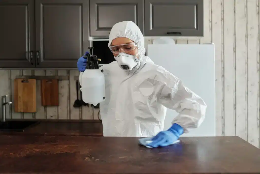 Personne portant des gants et un masque nettoyant une surface poussiéreuse dans un grenier