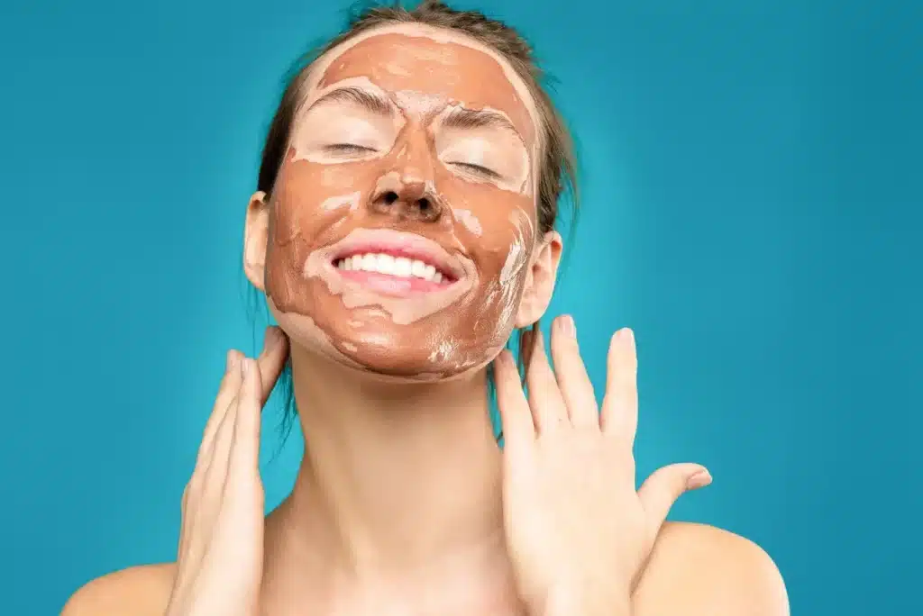 Mains appliquant un masque au miel doré sur le visage avec des ingrédients naturels à proximité