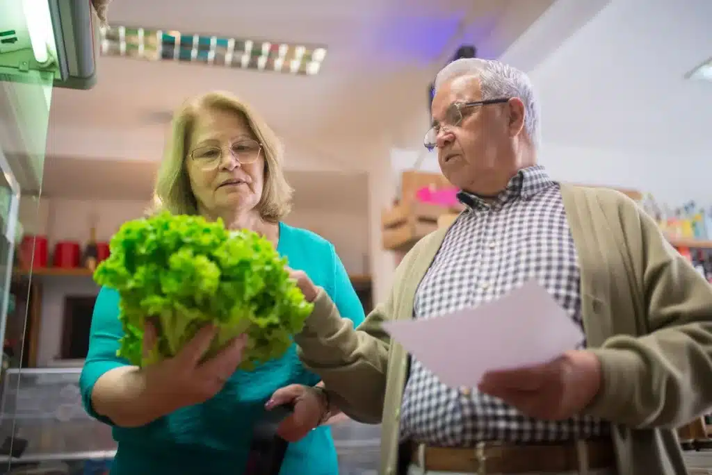 Mains d'une personne âgée préparant un repas équilibré avec légumes frais et féculents complets