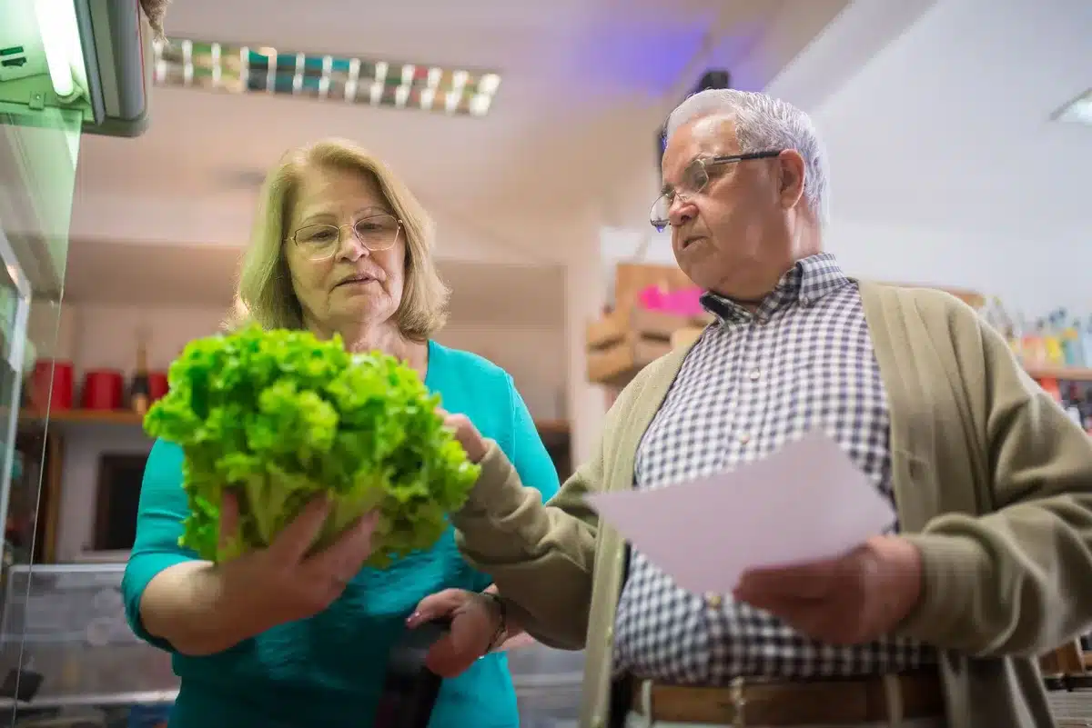 Mains d'une personne âgée préparant un repas équilibré avec légumes frais et féculents complets