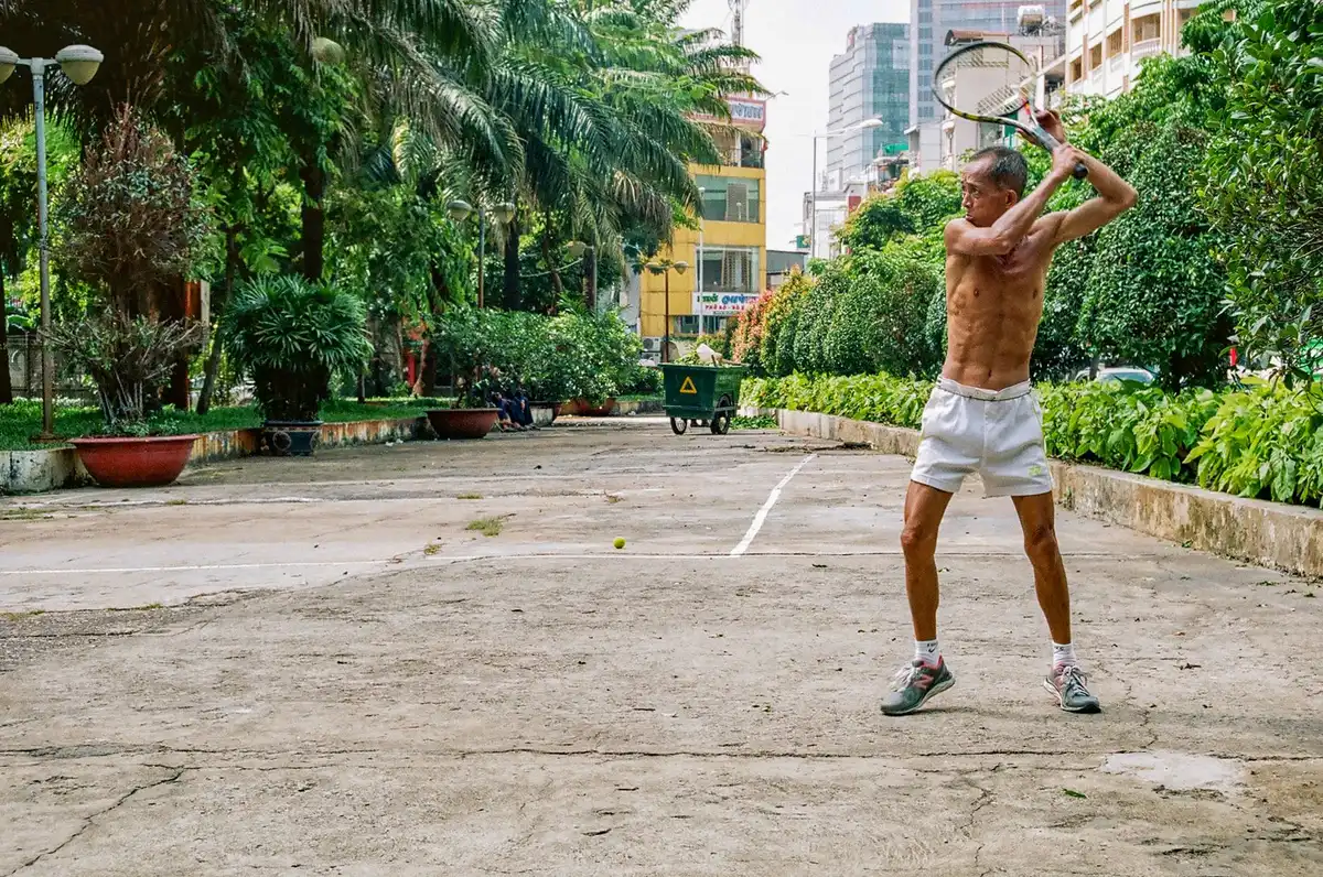 Personne âgée jouant au tennis sur un court, en position de jeu active.