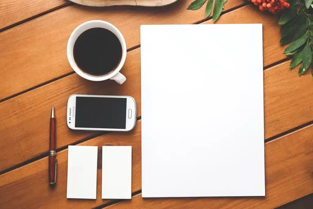 Mains d’un voyageur tenant une carte papier à côté d’un smartphone et d’un petit sac sur une table de café